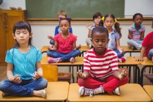 Pupils meditating in lotus position on desk in classroom at the